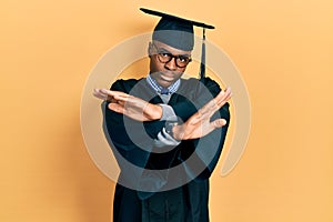 Young african american man wearing graduation cap and ceremony robe rejection expression crossing arms and palms doing negative
