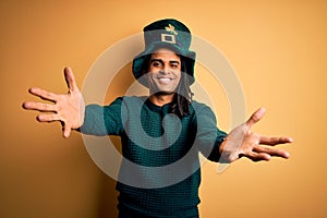 Young african american man wearing green hat with clover celebrating saint patricks day looking at the camera smiling with open