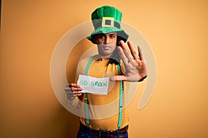 Young african american man wearing green hat holding banner celebrating saint patricks day with open hand doing stop sign with