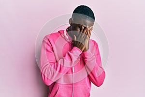 Young african american man wearing gym clothes and using headphones with sad expression covering face with hands while crying