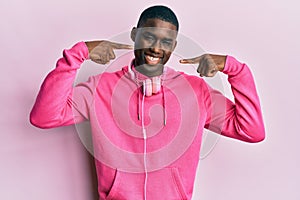 Young african american man wearing gym clothes and using headphones smiling cheerful showing and pointing with fingers teeth and