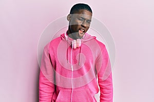 Young african american man wearing gym clothes and using headphones winking looking at the camera with sexy expression, cheerful