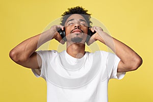 Young African American man wearing headphone and enjoy music over yellow gold Background