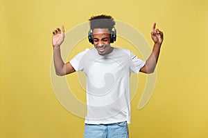 Young African American man wearing headphone and enjoy music over yellow gold Background