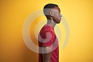 Young african american man wearing red t-shirt standing over isolated yellow background looking to side, relax profile pose with