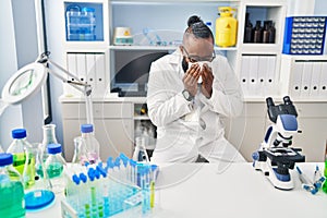 Young african american man wearing scientist uniform illness using napkin at laboratory