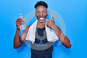 Young african american man wearing sportswear and towel holding bottle of water smiling happy and positive, thumb up doing