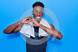 Young african american man wearing sportswear and towel smiling in love doing heart symbol shape with hands