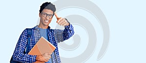 Young african american man wearing student backpack holding book approving doing positive gesture with hand, thumbs up smiling and