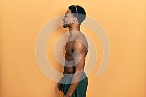 Young african american man wearing swimwear and swimmer glasses looking to side, relax profile pose with natural face and