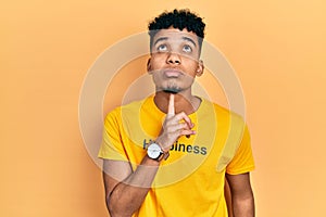 Young african american man wearing t shirt with happiness word message thinking concentrated about doubt with finger on chin and