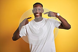 Young african american man wearing white t-shirt standing over isolated yellow background smiling cheerful showing and pointing