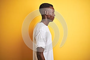 Young african american man wearing white t-shirt standing over  yellow background looking to side, relax profile pose with