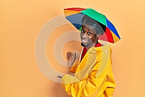 Young african american man wearing yellow raincoat inviting to enter smiling natural with open hand