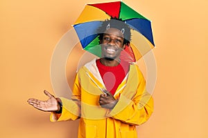 Young african american man wearing yellow raincoat showing palm hand and doing ok gesture with thumbs up, smiling happy and