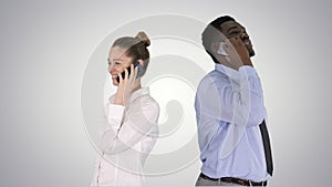 Young African American man and woman standing back to back making phone calls on gradient background.