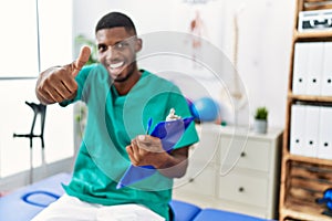 Young african american man working at pain recovery clinic approving doing positive gesture with hand, thumbs up smiling and happy