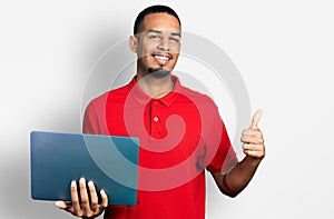 Young african american man working using computer laptop smiling happy and positive, thumb up doing excellent and approval sign