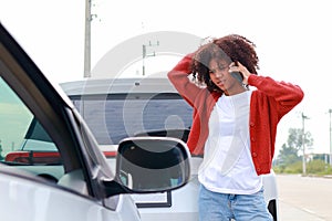 Young African American mixed race woman holding smartphone talking to car insurance company to notify for help.