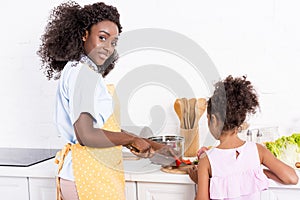 young african american mother and daughter cooking and cutting vegetables
