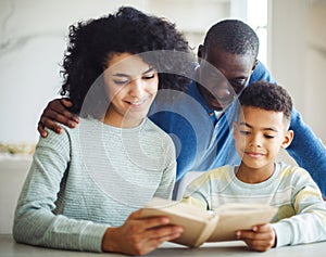 Young african american mother hold story book reading teaching little boy in living room. Father smiling.