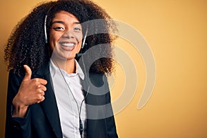 Young african american operator woman with afro hair wearing headset over yellow background doing happy thumbs up gesture with