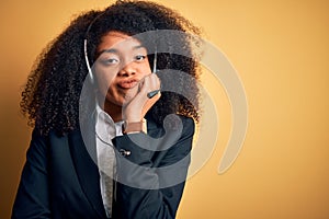 Young african american operator woman with afro hair wearing headset over yellow background thinking looking tired and bored with