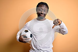 Young african american player man playing soccer holding football ball over yellow background with angry face, negative sign