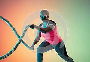 Young african-american plus size female model`s training on gradient background