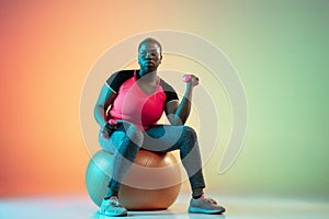 Young african-american plus size female model`s training on gradient background