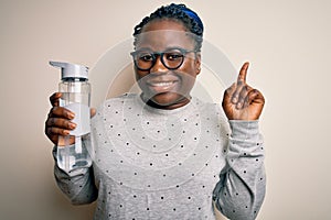 Young african american plus size sportswoman with braids drinking bottle of water surprised with an idea or question pointing