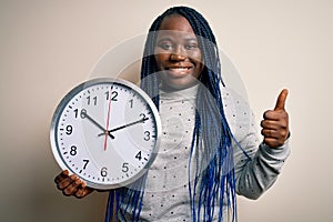 Young african american plus size woman with braids doing countdown holding big clock happy with big smile doing ok sign, thumb up