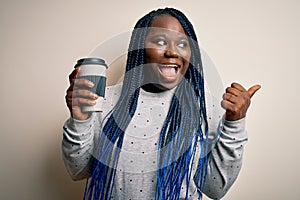 Young african american plus size woman with braids drinking cup of takeaway coffee pointing and showing with thumb up to the side