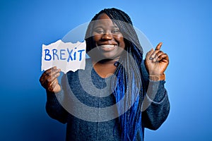 Young african american plus size woman with braids holding paper with brexit message surprised with an idea or question pointing