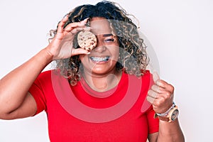 Young african american plus size woman holding cookie screaming proud, celebrating victory and success very excited with raised