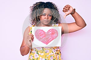 Young african american plus size woman holding heart shape paper with angry face, negative sign showing dislike with thumbs down,