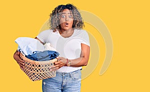 Young african american plus size woman holding laundry basket scared and amazed with open mouth for surprise, disbelief face