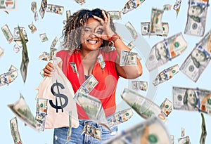 Young african american plus size woman holding money bag with dollar symbol smiling happy doing ok sign with hand on eye looking