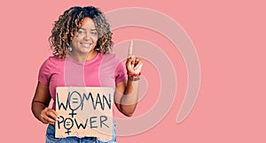 Young african american plus size woman holding woman power banner surprised with an idea or question pointing finger with happy