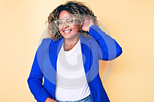 Young african american plus size woman wearing business jacket and glasses smiling with hand over ear listening and hearing to