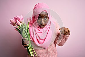 Young african american plus size woman wearing muslim hijab holding bouquet of pink tulips Pointing down with fingers showing