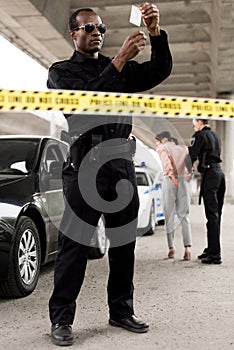 young african american policeman in sunglasses holding plastic zipper with drugs while his partner arresting photo