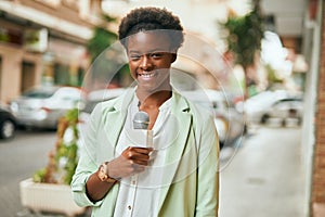 Young african american reporter woman using microphone at the city