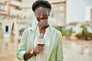 Young african american reporter woman using microphone at the city