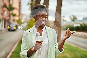 Young african american reporter woman using microphone at the city