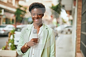 Young african american reporter woman using microphone at the city