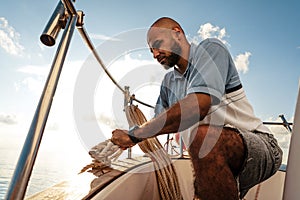 Young african american sailor tying ropes on sailboat in the sea on sunset