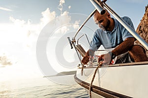 Young african american sailor tying ropes on sailboat in the sea on sunset