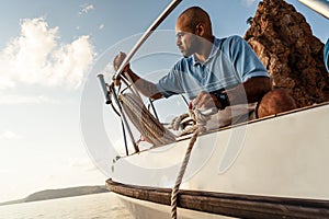 Young african american sailor tying ropes on sailboat in the sea on sunset