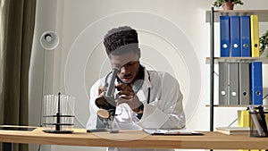 Young african american scientist looking through a microscope in a laboratory